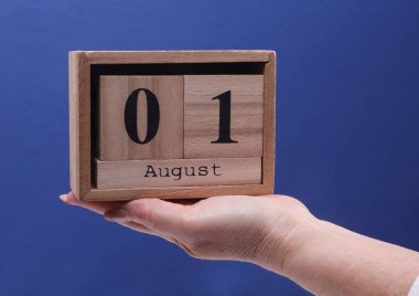 1 Ağustos tarihli ahşap blok takvimi taşıyan Kadın El mavi bir arkaplanda