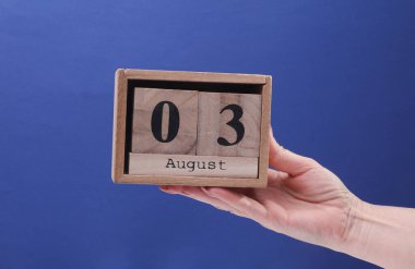3 Ağustos tarihli ahşap blok takvimi taşıyan Kadın El mavi arka planda