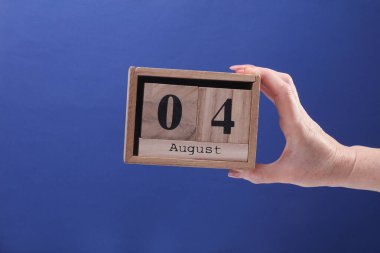 4 Ağustos tarihli ahşap blok takvimi tutan kadın el mavi arka planda