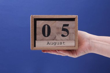 5 Ağustos tarihli ahşap blok takvimi tutan kadın el mavi arka planda