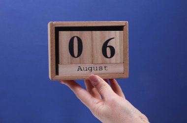 6 Ağustos tarihli ahşap blok takvimi tutan kadın el mavi arka planda