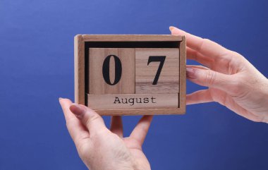 Kadın El, elinde tahta blok takvimi ile 7 Ağustos tarihli mavi arkaplan üzerinde