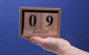 9 Ağustos tarihli ahşap blok takvimi tutan kadın el mavi arka planda