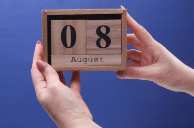 Bayan El ahşap blok takvimi tutuyor ve tarih 8 Ağustos, mavi bir arkaplan.