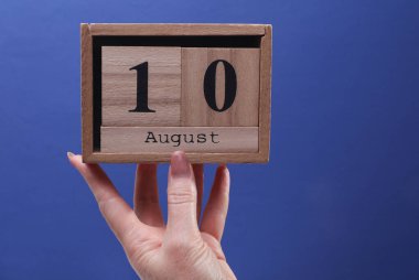 10 Ağustos tarihli ahşap blok takvimi tutan kadın el mavi arka planda