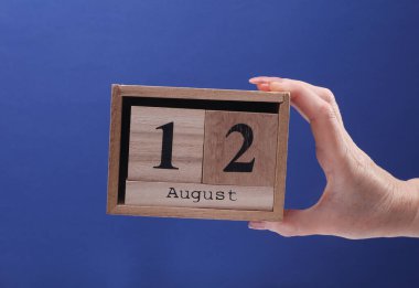 12 Ağustos tarihli ahşap blok takvimi tutan kadın el mavi arka planda