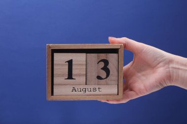 13 Ağustos tarihli ahşap blok takvimine mavi arka planda sahip kadın el.