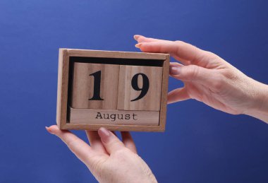 Kadın El ahşap blok takvimi tutuyor ve tarih 19 Ağustos, mavi zemin üzerinde.