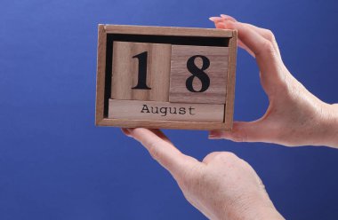 18 Ağustos tarihli ahşap blok takvimi tutan kadın el mavi arka planda.