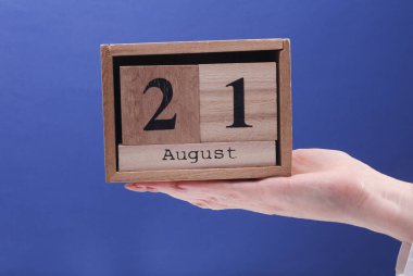 21 Ağustos tarihli ahşap blok takvimi tutan kadın el mavi arka planda