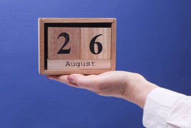 26 Ağustos tarihli ahşap blok takvimi tutan kadın el mavi arka planda.