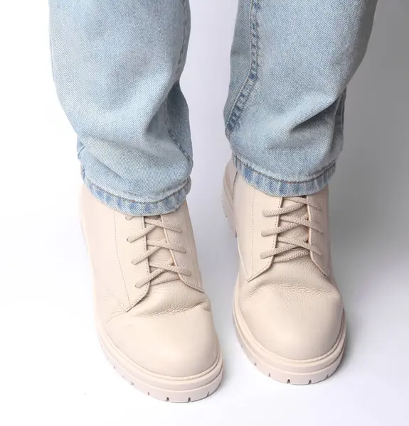 Kot pantolonlu kadın bacakları ve beyaz arka planda beyaz deri çizmeler. Moda konsepti