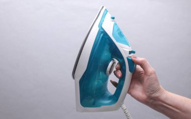 Gri arka planda ütü yapmak için ütü tutan kadın el.