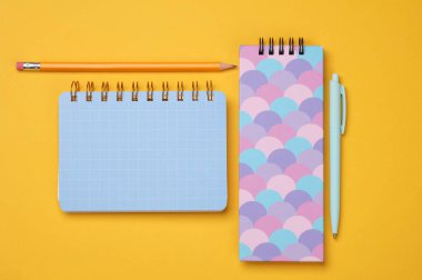 Sarı arka planda kalemleri olan not defterleri. Üst görünüm