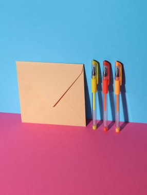 Mavi-pembe pastel arka planda renkli kalemlerle zarf