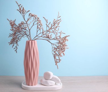 İskandinav tarzında minimalist vazo. Kurumuş çiçekler, alçı tepsi ve masada taşlar, mavi arkaplan.