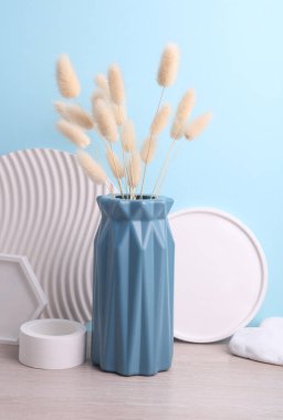 İskandinav tarzında minimalist vazo. Masada kurumuş lagurus çiçeği ve alçı tepsiler var. Mavi arka plan.