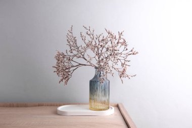 Gri arka planda kurumuş çiçekli cam vazo.