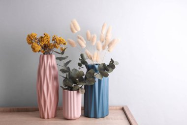 Ahşap masa üzerinde kuru çiçekli vazolar, gri arkaplan