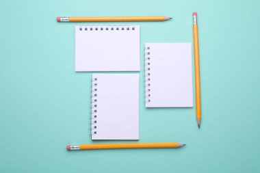 Nane yeşili arka planda kalemleri olan boş beyaz spiral defterler