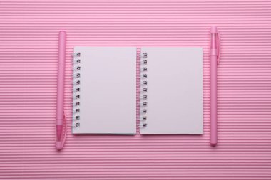 Pembe arka planda iki beyaz sarmal defter ve kalem.