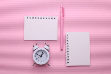 Pembe arka planda çalar saat olan boş, sarmal defterler. İş konsepti