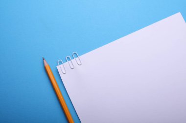 Mavi zemin üzerinde ataç ve kalem olan beyaz kağıt.