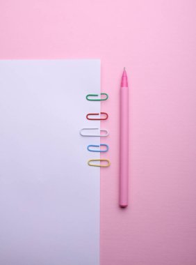 Renkli ataçları ve pembe arka planda kalemi olan beyaz kağıt.