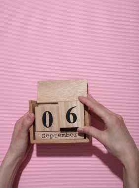 Elleri ahşap blok takviminde, tarihi Eylül 06 pembe arka planda.