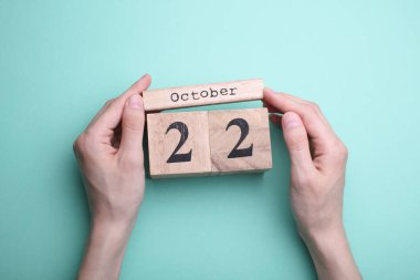 Nane yeşili arkaplanda 22 Ekim tarihli ahşap blok takvimi tutan eller