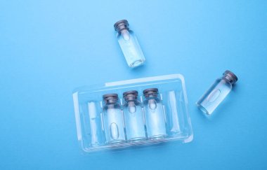 Mavi arka planda sıvı bulunan tıbbi cam şişeler.