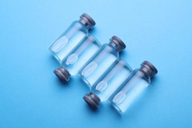 Mavi arka planda sıvı bulunan tıbbi cam şişeler.