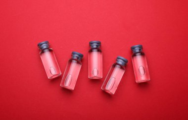 Kırmızı zemin üzerinde sıvı olan tıbbi cam şişeler.