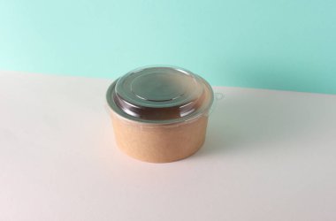 Masanın üzerinde plastik kapaklı karton yuvarlak yemek kutusu, turkuaz arka plan