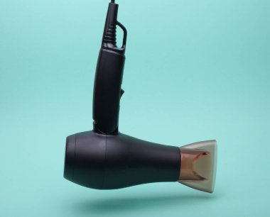 Nane yeşili arkaplanda yüzen siyah saç kurutma makinesi