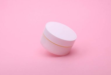 Pembe arka planda yüzen beyaz krema kavanozu.