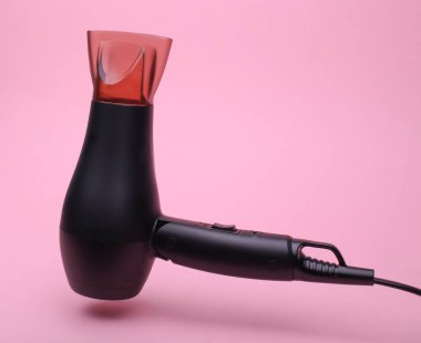 Pembe arka planda yüzen siyah saç kurutma makinesi.