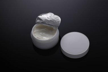 Siyah zemin üzerinde beyaz açık krema kavanozu ve yansıması