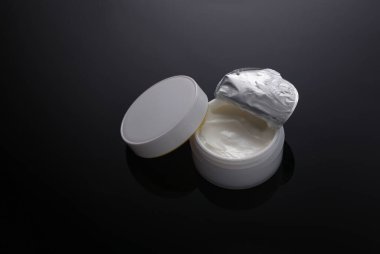 Siyah zemin üzerinde beyaz açık krema kavanozu ve yansıması