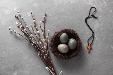 Easter eggs in nest with Christian cross and pussy willow branches on grey concrete background. Top view