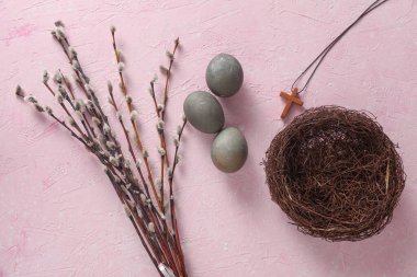 Easter eggs, nest with Christian cross and pussy willow branches on pink concrete background. Top view