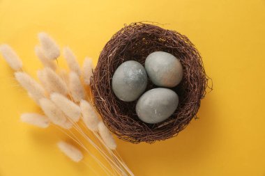 Sarı arka planda lagugrus çiçekleri olan Paskalya yumurtaları yuvada