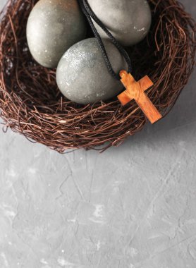 Yuvasında Paskalya yumurtaları ve gri beton arka planda Hıristiyan haçı.