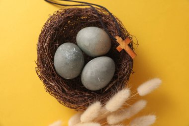 Yuvasında Hıristiyan haçı ve sarı arka planda lagurus çiçekleri olan Paskalya yumurtaları. Üst görünüm
