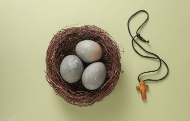 Yuvasında Paskalya yumurtaları ve yeşil arka planda Hıristiyan haçı. Üst görünüm