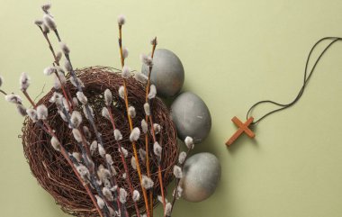 Easter eggs in nest with Christian cross and pussy willow branches on green background. Top view