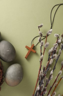 Easter eggs in nest with Christian cross and pussy willow branches on green background. Top view