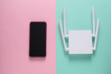 Modern dört antenli kablosuz ağ yönlendirici ve pembe arka planda akıllı telefon. Üst görünüm