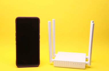 Sarı arka planda akıllı telefonu olan modern beyaz dört antenli Wi-Fi yönlendirici.