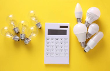 Sarı arka planda hesap makinesi olan LED ve parlak ampuller. Elektrik tasarrufu